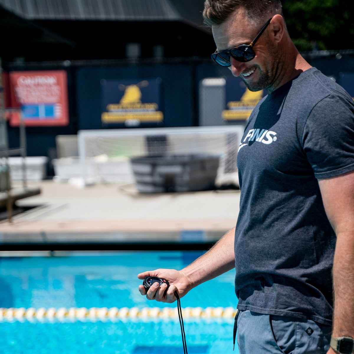 Swimming coach using FINIS 3X100M Stopwatch to monitor performance from pool deck