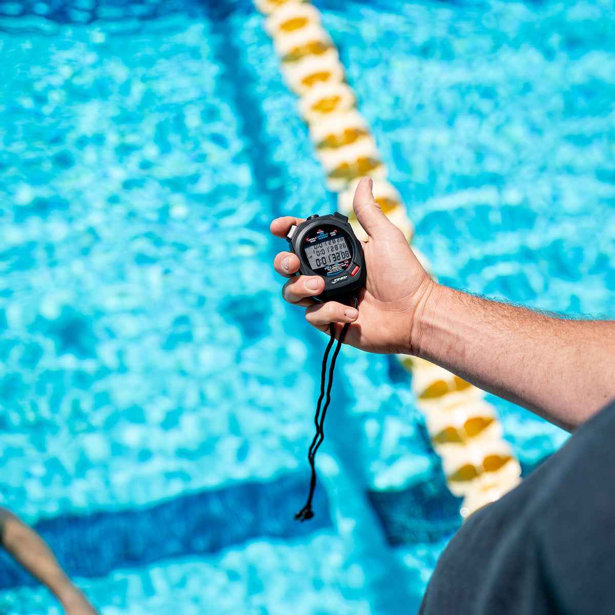 Close-up of coach's hand holding FINIS 3X100M Stopwatch above pool lane