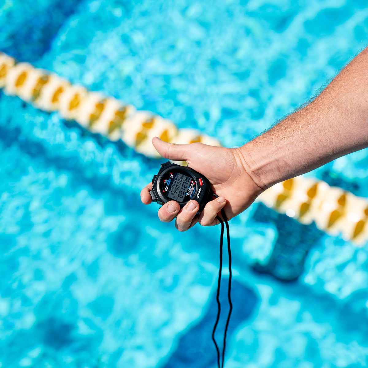 Coach gripping FINIS 3X100M Stopwatch during lap timing over swimming lane