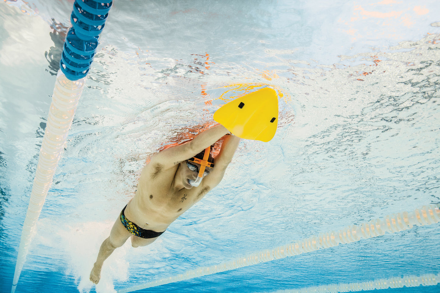 Side underwater view of swimmer holding FINIS yellow kickboard for alignment training