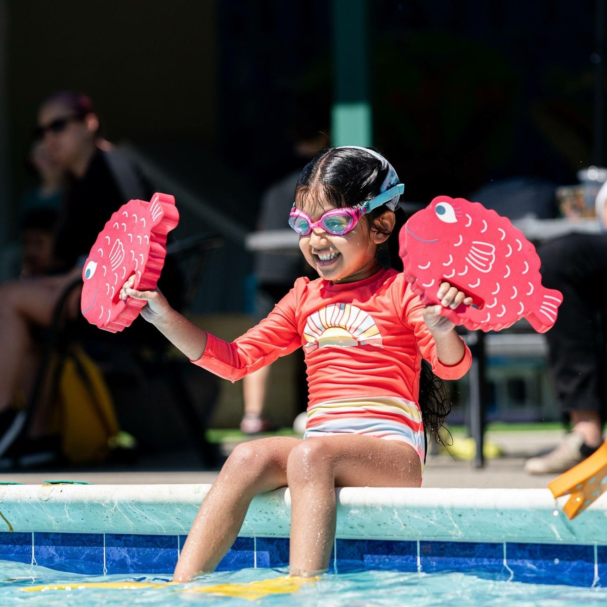 Child sitting by pool holding FINIS Floatie Friends pufferfish foam floats