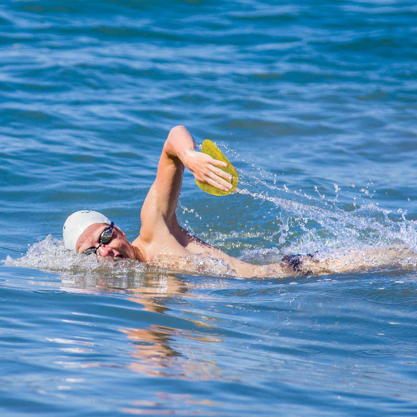 Male swimmer using FINIS Agility Paddle for freestyle drills in open water environment.