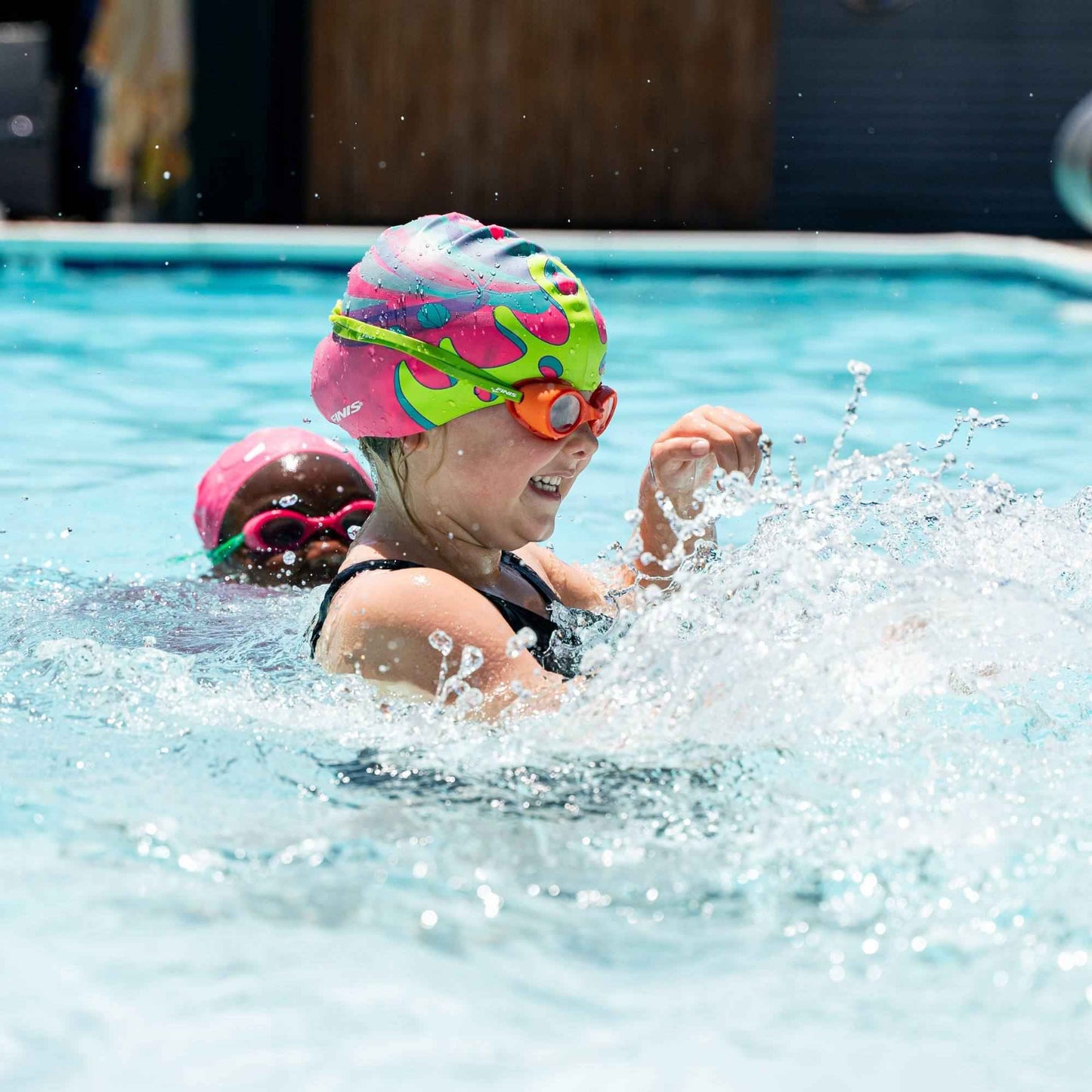 Young swimmer in FINIS Orange goggles splashing water during swim class