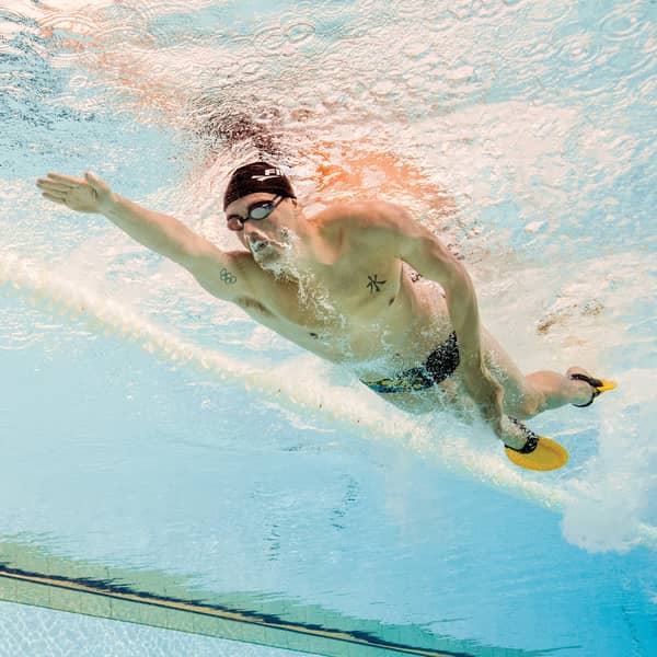 Man swimming underwater in a pool with a swim cap and goggles.