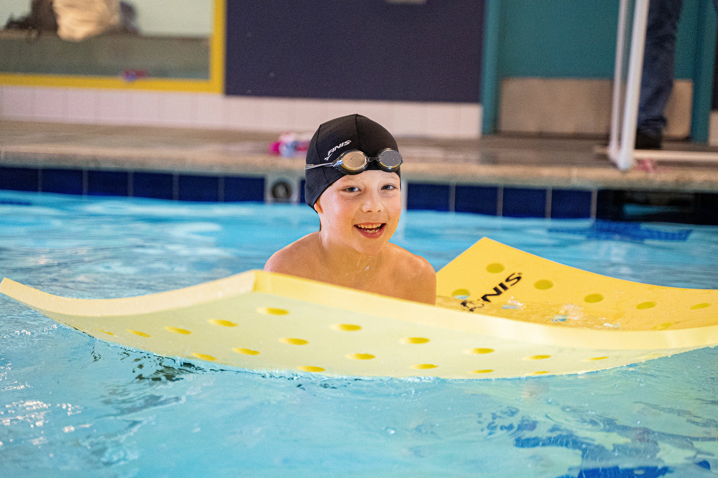 Boy in indoor pool using FINIS Racer Ripple goggles while floating on yellow swim board
