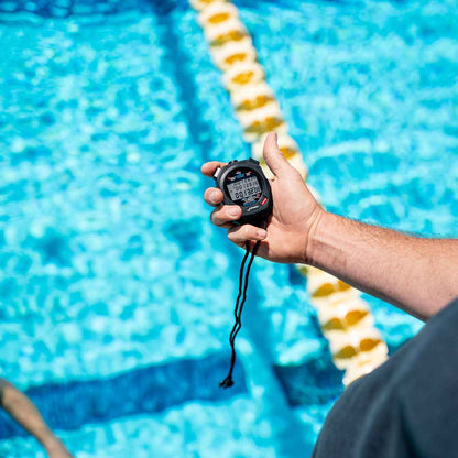 Close-up of coach's hand holding FINIS 3X100M Stopwatch above pool lane