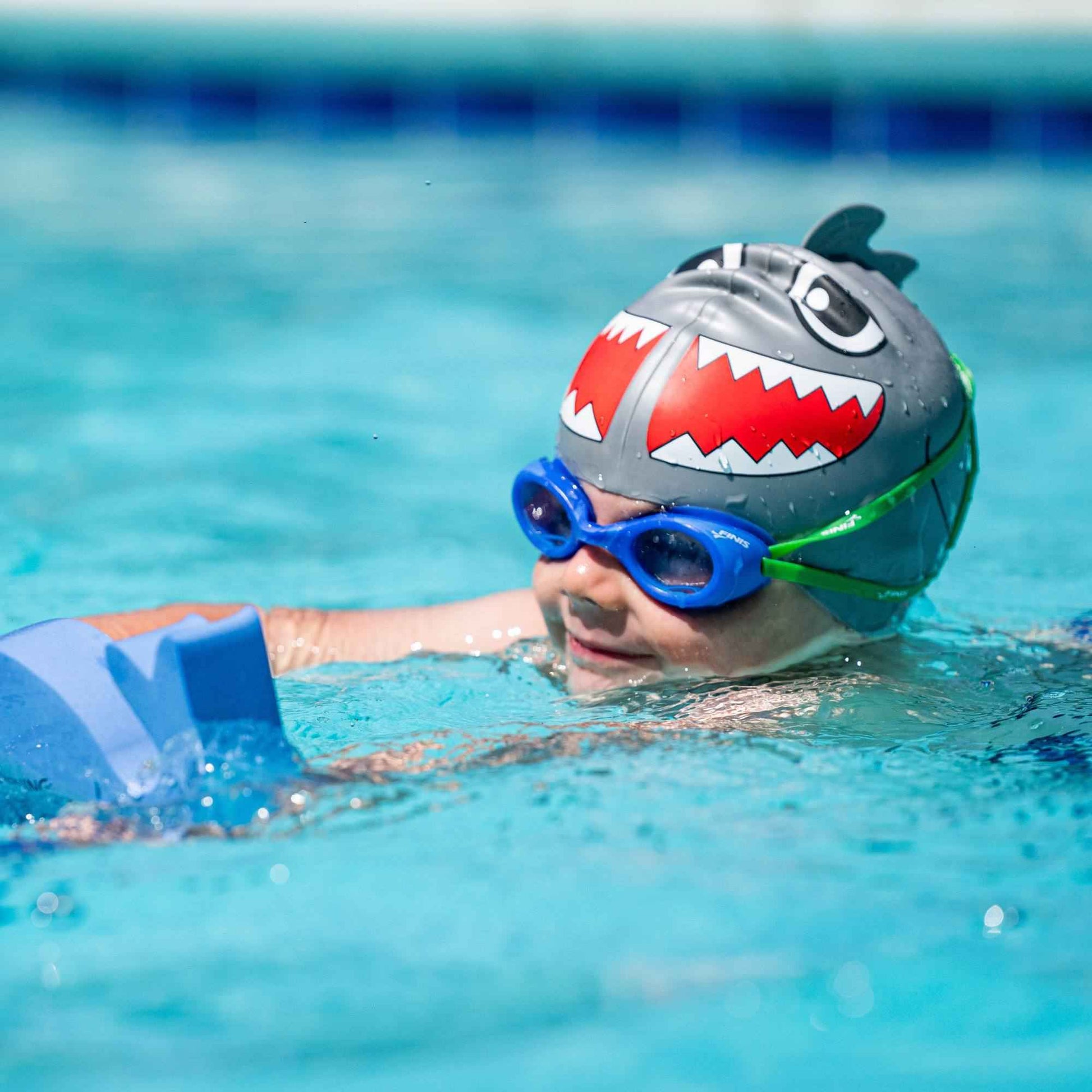 Child wearing FINIS Blueberry scented swim goggles while swimming with kickboard