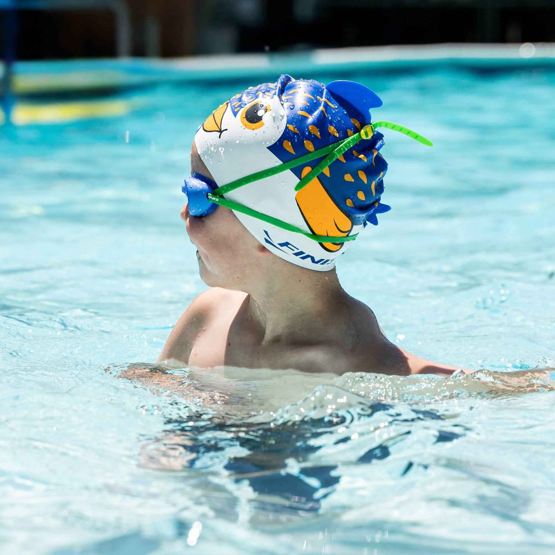 Young swimmer wearing FINIS Blueberry goggles and fish cap, looking sideways in pool