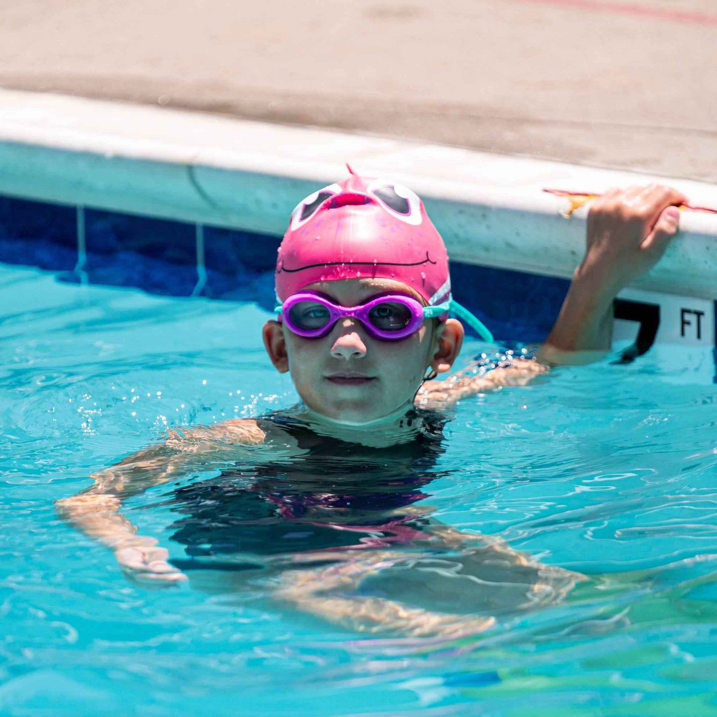 Young swimmer wearing FINIS Grape goggles resting at the pool edge