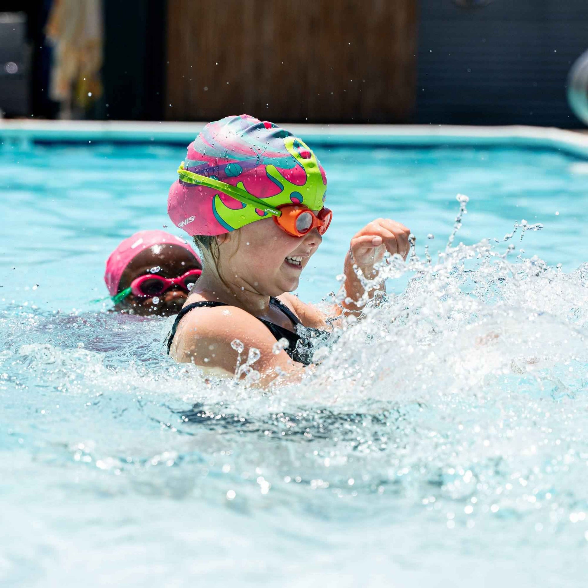 Young swimmer in FINIS Orange goggles splashing water during swim class