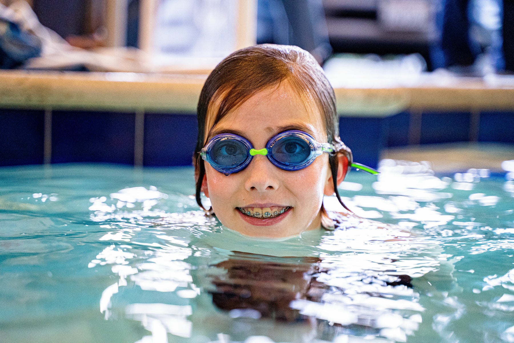 Close-up of smiling girl in pool wearing FINIS Racer Ripple goggles with blue lenses